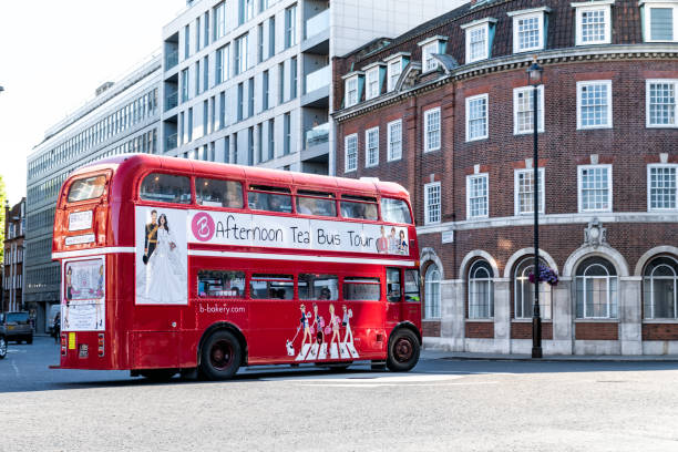 London, UK - June 22, 2018: Iconic, classic red double decker bus driving, turning on intersection with people sitting, eating during Afternoon Tea Tour