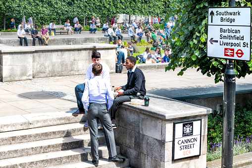 London, UK - June 22, 2018: Young three businessmen sitting in Festival Gardens by St Paul's Cathedral, Cannon Street, churchyard during lunch break, talking