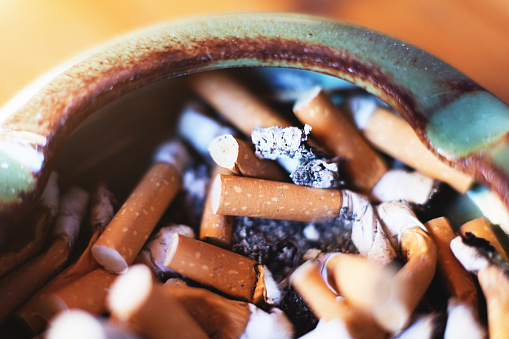 A ceramic ashtray is crammed with fag ends, the remains of smoked filter cigarettes.