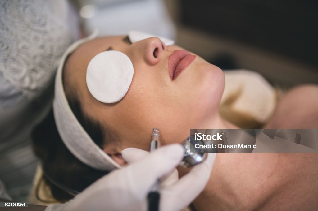 Young woman with a towel on her head lying on a table with closed eyes getting a laser skin treatment in healthy beauty spa salon Close-up top-view side-view portrait of a young woman with a towel on her head lying on a table with closed eyes getting a laser skin treatment in healthy beauty spa salon Laser Stock Photo