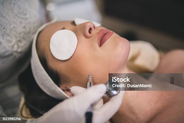 Young Woman With A Towel On Her Head Lying On A Table With Closed Eyes Getting A Laser Skin Treatment In Healthy Beauty Spa Salon Stock Photo - Download Image Now