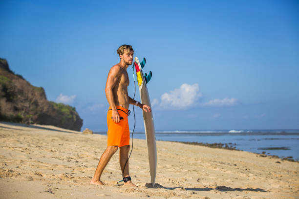 istock side view of young man with surfing board on sandy beach near ocean 1023992014