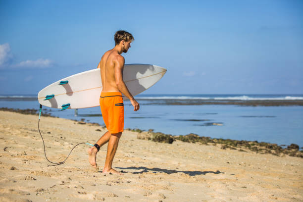 istock young athletic sportsman with surfing board walking on sandy beach 1023992038