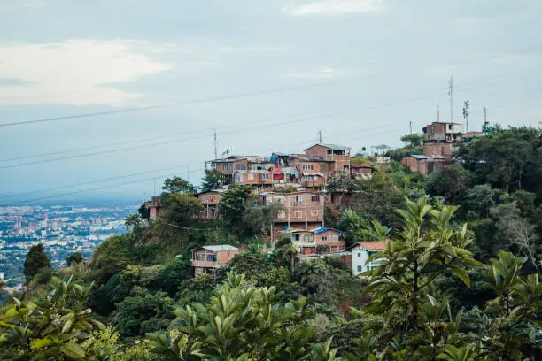 Shanty town homes in Colombia overlooking other buildings and houses in Colombia surrounded by nature. Copy space available, cloudy day, wires strung across the image.