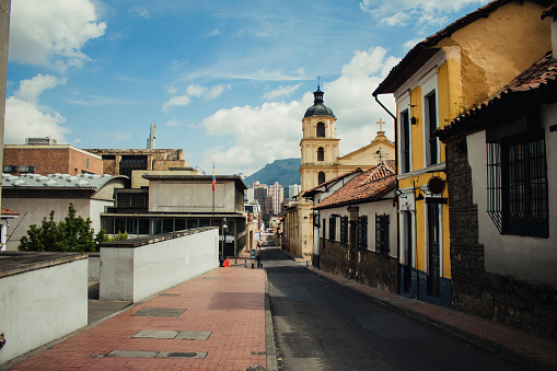 A downhill view shot following a straight road down a colombian street, colourful houses and a church, plus more modern buildings.
