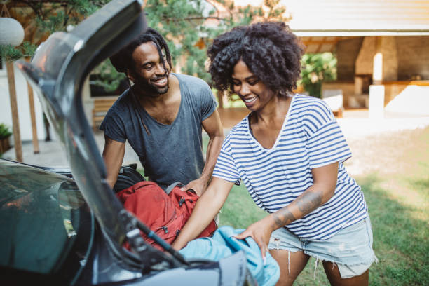 Couple loading a car. Young African-American couple loading/unloading a car. Putting backpacks in open trunk. city break photos stock pictures, royalty-free photos & images