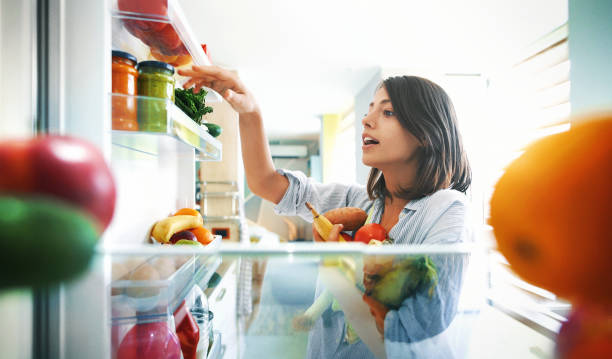 Woman picking up some fruits and veggies from the fridge Closeup of a cheerful young couple picking some fruit and veggies from the fridge to make some healthy breakfast on Sunday morning. Shot from inside the working fridge. vegan food photos stock pictures, royalty-free photos & images