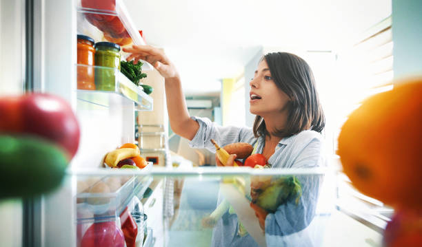 Woman picking up some fruits and veggies from the fridge Closeup of a cheerful young couple picking some fruit and veggies from the fridge to make some healthy breakfast on Sunday morning. Shot from inside the working fridge. insides stock pictures, royalty-free photos & images