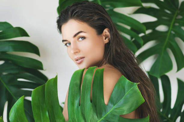 Portrait of young and beautiful woman with perfect smooth skin in tropical leaves Portrait of young and beautiful woman with perfect smooth skin in tropical leaves. Concept of natural cosmetics and skincare. woman smooth hair stock pictures, royalty-free photos & images