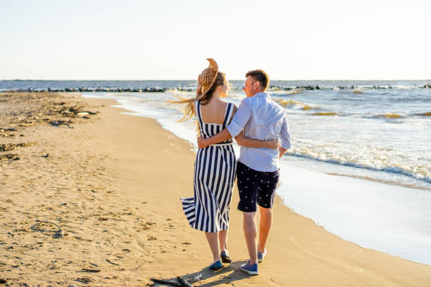 istock rear view of affectionate couple walking on sandy beach on summer day 1024092716
