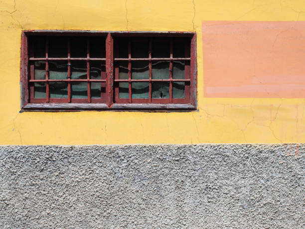 古い塗られた黄色と灰色コンクリート壁バーと苦しめられたひび割れテクスチャ狭い赤のフレーム ウィンドウと - patched brick pattern textured ストックフォトと画像