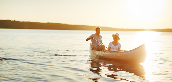 Smiling young man paddling a canoe on a lake with his girlfriend looking at the scenery on a late summer afternoon