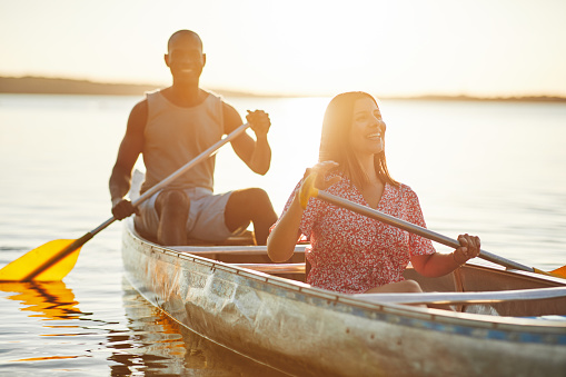 Smiling young woman and her boyfrind paddling a canoe together on a lake on a sunny summer afternoon