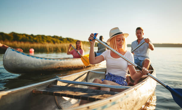 sonriente mujer joven piragüismo con amigos en una tarde soleada - kayak canoeing canoe lake fotografías e imágenes de stock