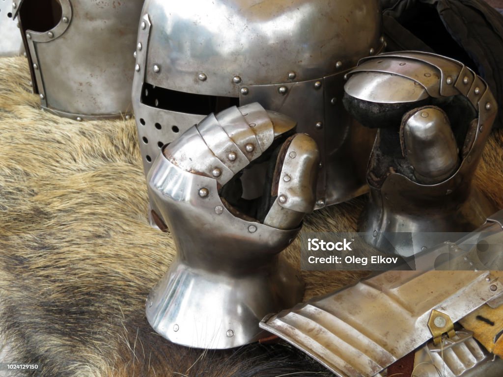 Medieval helmets and gloves on a bearskin rug Armor of middle ages, knightly equipment, armory forge Ancient Stock Photo