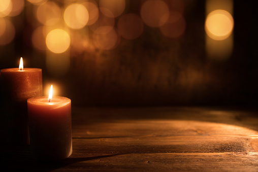 Burning candles and festive golden bokeh on dark wood