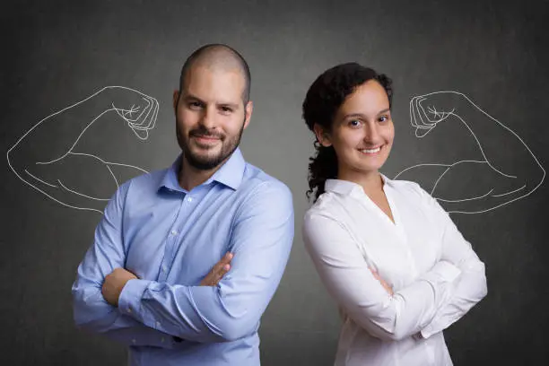 Business Team with muscular arms standing in front of a grey blackboard background. Concept of team-building and motivated young colleagues.