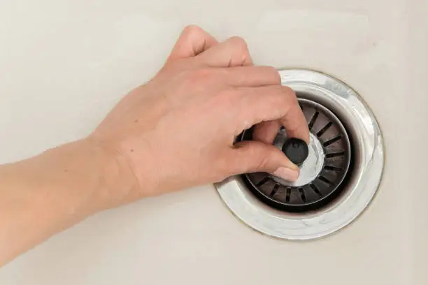 Woman hand pulls close cap of drainage hole of sink to drain water