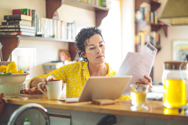 Mature woman is checking her finances at home Mature woman is checking her finances at home one mature woman only stock pictures, royalty-free photos & images