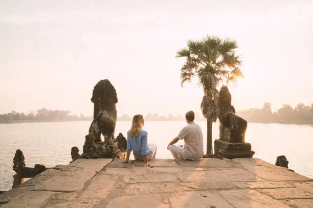 Photo of Young couple contemplating ancient temple by the lake in Cambodia , Sunrise, people travel discovery couple romance concept