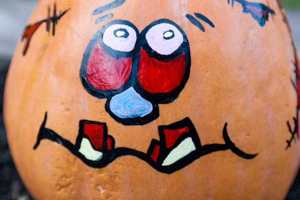 A close-up shot shows a cheerfully painted Halloween pumpkin, surrounded by art supplies and the female hands who are creating festive decor.