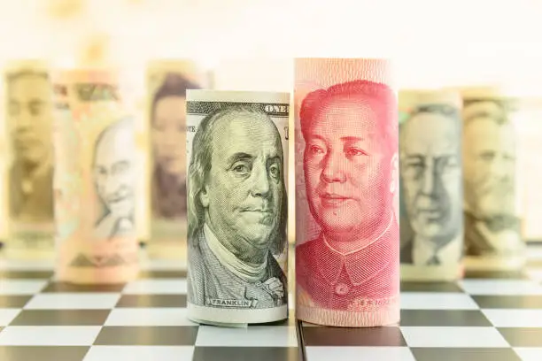 World economy and forex / foreign currency exchange concept : Rolled up scroll of USD US dollar and CNY Chinese yuan banknotes with portrait of Benjamin Franklin and Mao Zedong on a square chessboard.