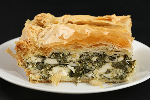 A macro, horizontal photograph of a white place with a portion of Spanakopita. Isolated on black