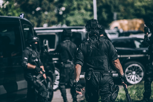 Group of men, special forces armed team, standing by police vehicles, ready for action.