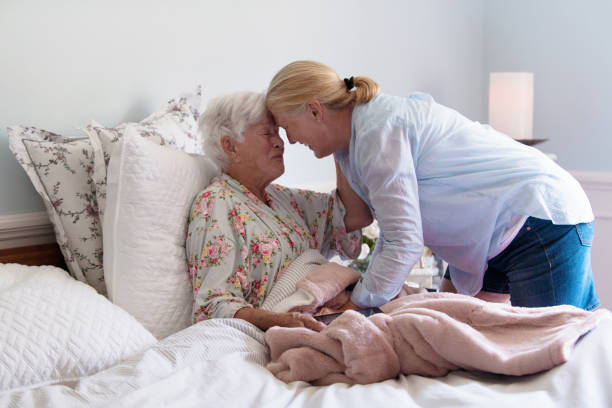 A senior woman in her bed embracing her daughter with emotion A senior woman of 85 years old embracing her daughter with emotion.  The lady wear a flower pyjama. She have gray hair. She is in the bedroom. Photo was taken in Quebec Canada during summer time. hospice photos stock pictures, royalty-free photos & images