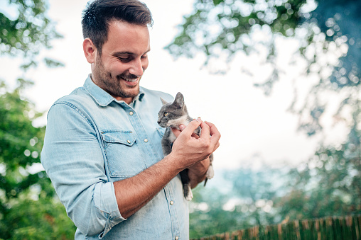Handsome man is holding and hugging cute cat outdoors.