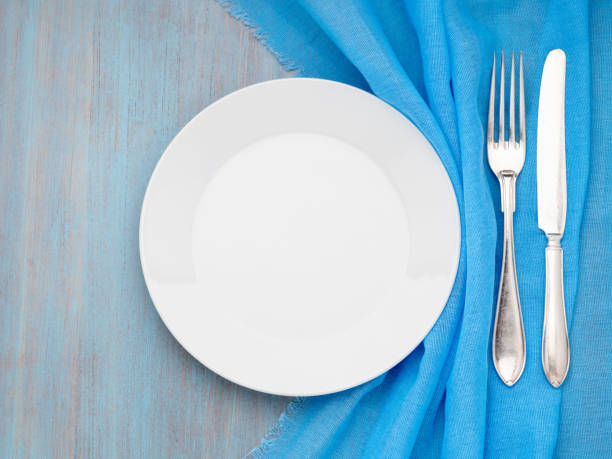 istock Blank flat white plate, fork, knife on blue wooden table, top view. Mock up, concept for marine restaurant, fish menu 1024230072