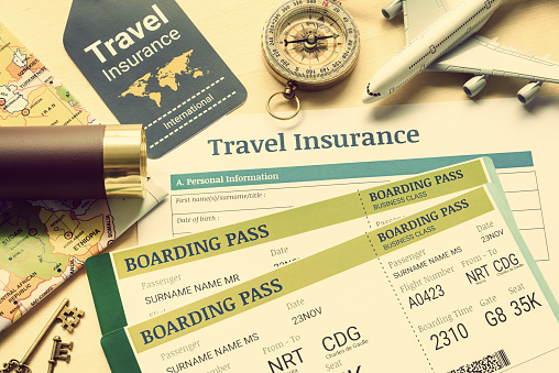 Travel insurance and travel security service concept : Top view of travel insurance application form, business class boarding passes, map, monocular, tag, compass, white model air plane on wood floor.