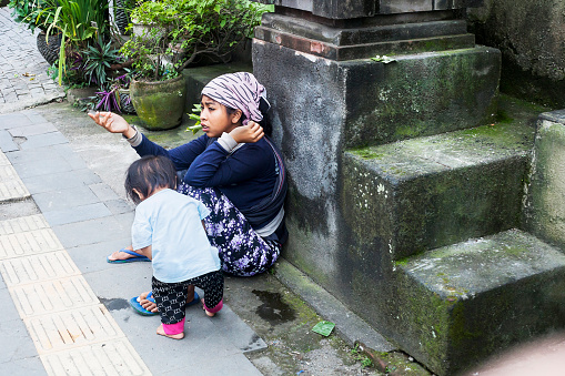 Ubud, Bali, Indonesia - 05 March 2018: Beggar woman with small child on street begging for alms