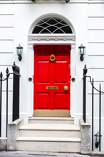 Facade of an old classic typical residential building with a red door on a white wall in London, England, United Kingdom