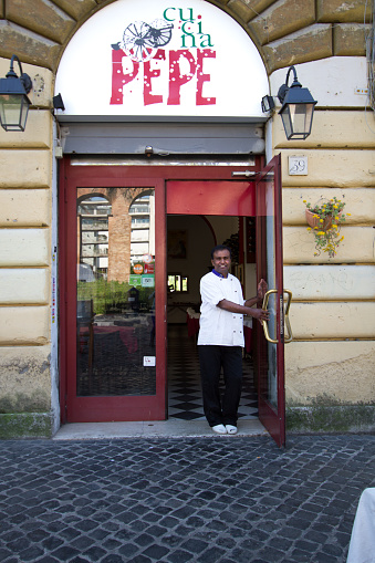 Rome, Italy: A chef in chef’s whites stands smiling in the doorway of a restaurant in the San Lorenzo neighborhood of Rome.