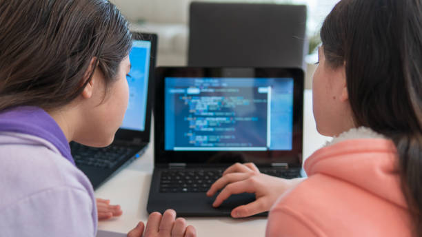 Girls learning to code on laptop computers at home stock photo