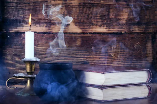 Photo of Old books of magic and witch pot with smoke and candle