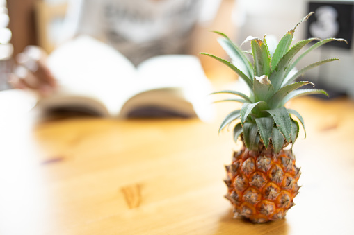 Composition with delicious small pineapple   on wooden beach table.People read book blur.