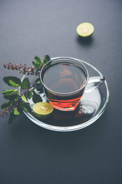 pouring Holy Basil or Tulsi Tea in transparent glass cup with saucer over white or black background. Popular Ayurvedic medicine from India stock photo