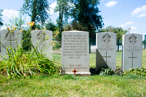 Four Graves and a plaque of soldiers that died as prisoner of war, who's graves have now been lost. The regiment of each solidier can be seen on the tombstone. A little cross with a poppy is also visible in the front of the plaque. These graves are in the ST Symphorien Military Cemetery in Mons.