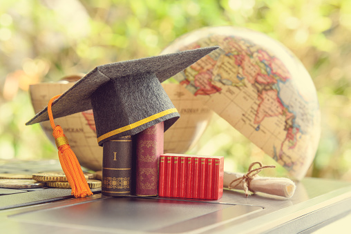 Key success in graduate study abroad program and open or expand world view experience concept : Graduation cap or hat, certificate or diploma, mini text books on a laptop computer, a half world globe.