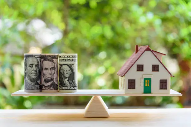 Photo of Home loan / reverse mortgage or transforming assets into cash concept : House model, US dollar notes on a simple balance scale, depicts a homeowner or a borrower turns properties / residence into cash