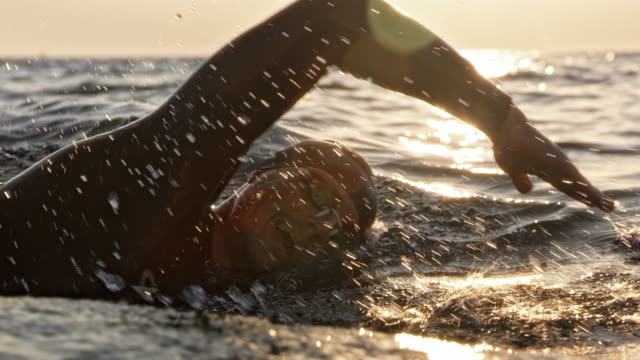 男性のオープンウォータースイマーが泳いでいるスローモーションメディア追跡ショットは、日差しの中で海を這います。スロベニアで撮影。