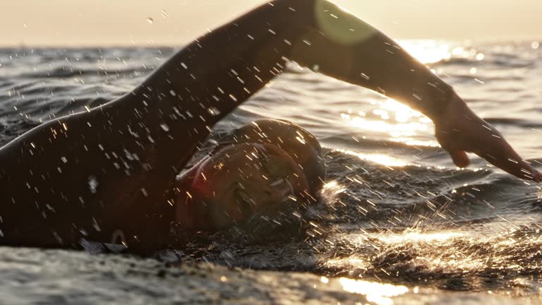 Slow motion medium tracking shot of a male open water swimmer swimming front crawl at sea in sunshine. Shot in Slovenia.