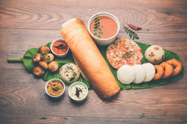 Photo of Group of South Indian food like Masala Dosa, Uttapam, Idli/idly, Wada/vada, sambar, appam, semolina halwa, upma served over banana leaf with colourful chutneys, selective focus