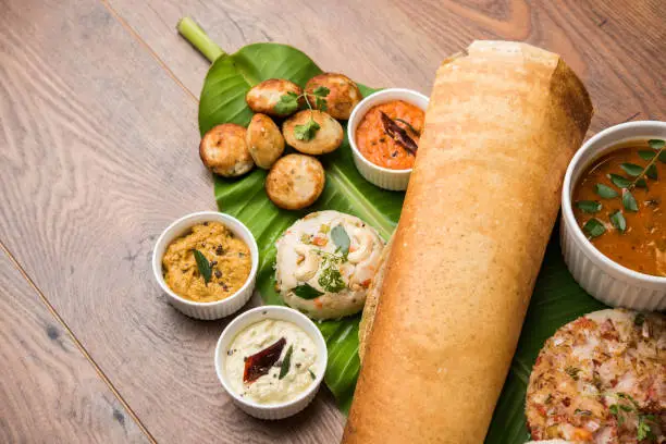 Photo of Group of South Indian food like Masala Dosa, Uttapam, Idli/idly, Wada/vada, sambar, appam, semolina halwa, upma served over banana leaf with colourful chutneys, selective focus