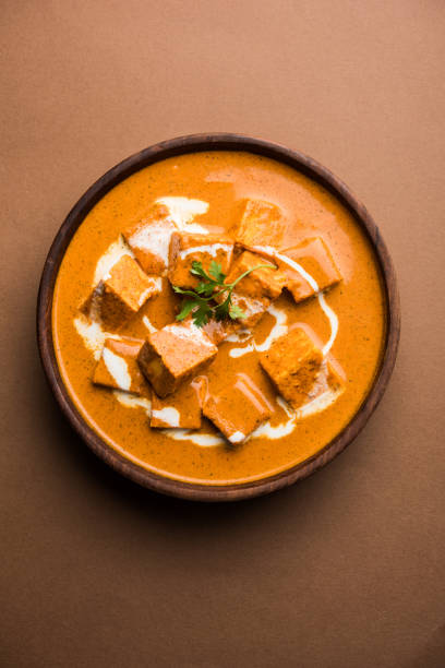 Paneer Butter Masala also known as Panir  makhani or makhanwala. served in a ceramic or wooden bowl with fresh cream and coriander. Isolated over colourful moody background. selective focus stock photo
