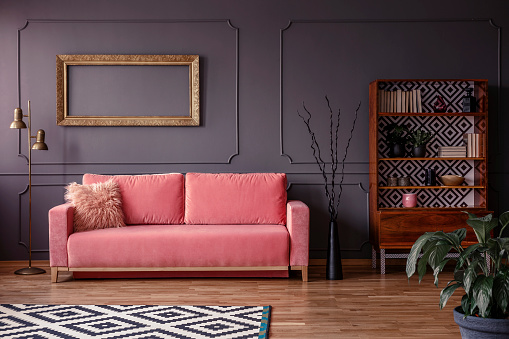 Pink settee against grey wall with mockup of gold frame in elegant living room interior. Real photo