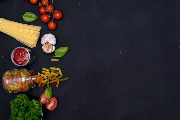 Food frame. Pasta ingredients. Cherry-tomatoes, spaghetti pasta, garlic, basil , cheese and spices on dark grunge backdrop, copy space, top view