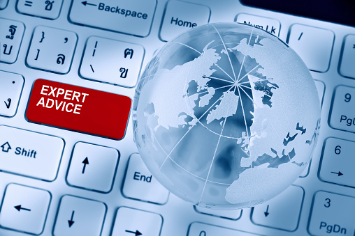 Expert advice and support service concept : Two words EXPERT ADVICE inscribed on a red enter key button of a white desktop computer keyboard decorated with a crystal clear globe and opaque world map.